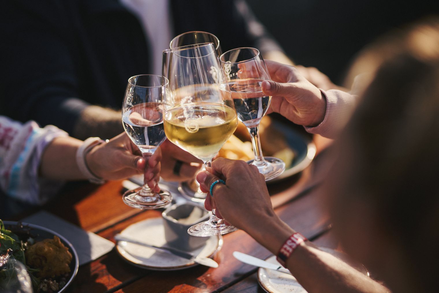 Menschen stoßen mit Wein- und Wassergläsern an einem gedeckten Tisch an