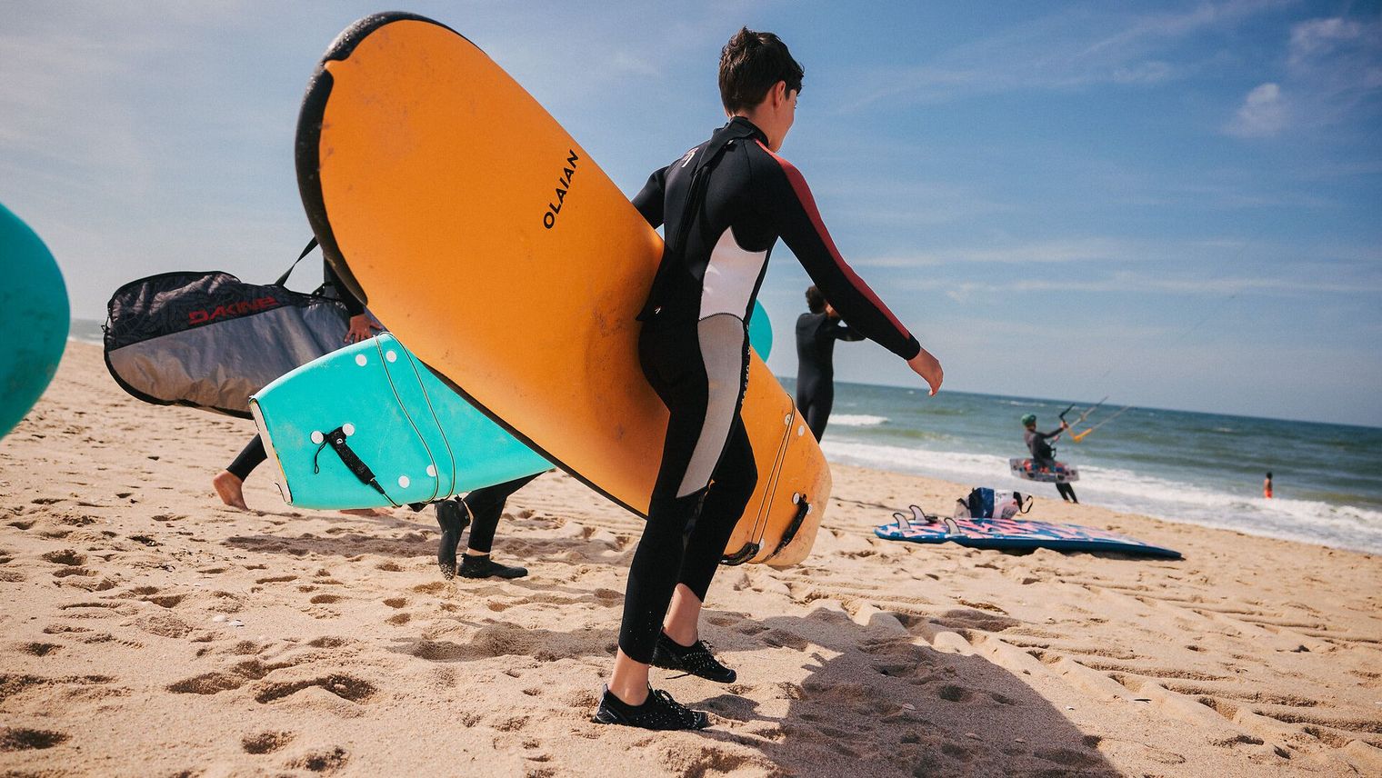 Jugendliche tragen bunte Surfboards am Strand in Richtung Meer.
