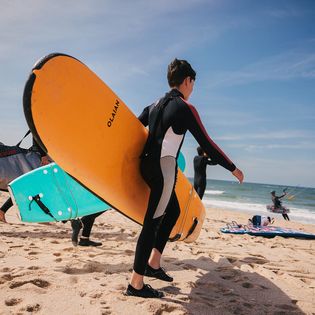 Jugendliche tragen bunte Surfboards am Strand in Richtung Meer.