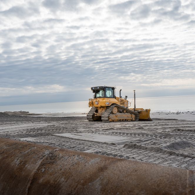 Ein Bagger verteilt den angespülten Sand am Strand