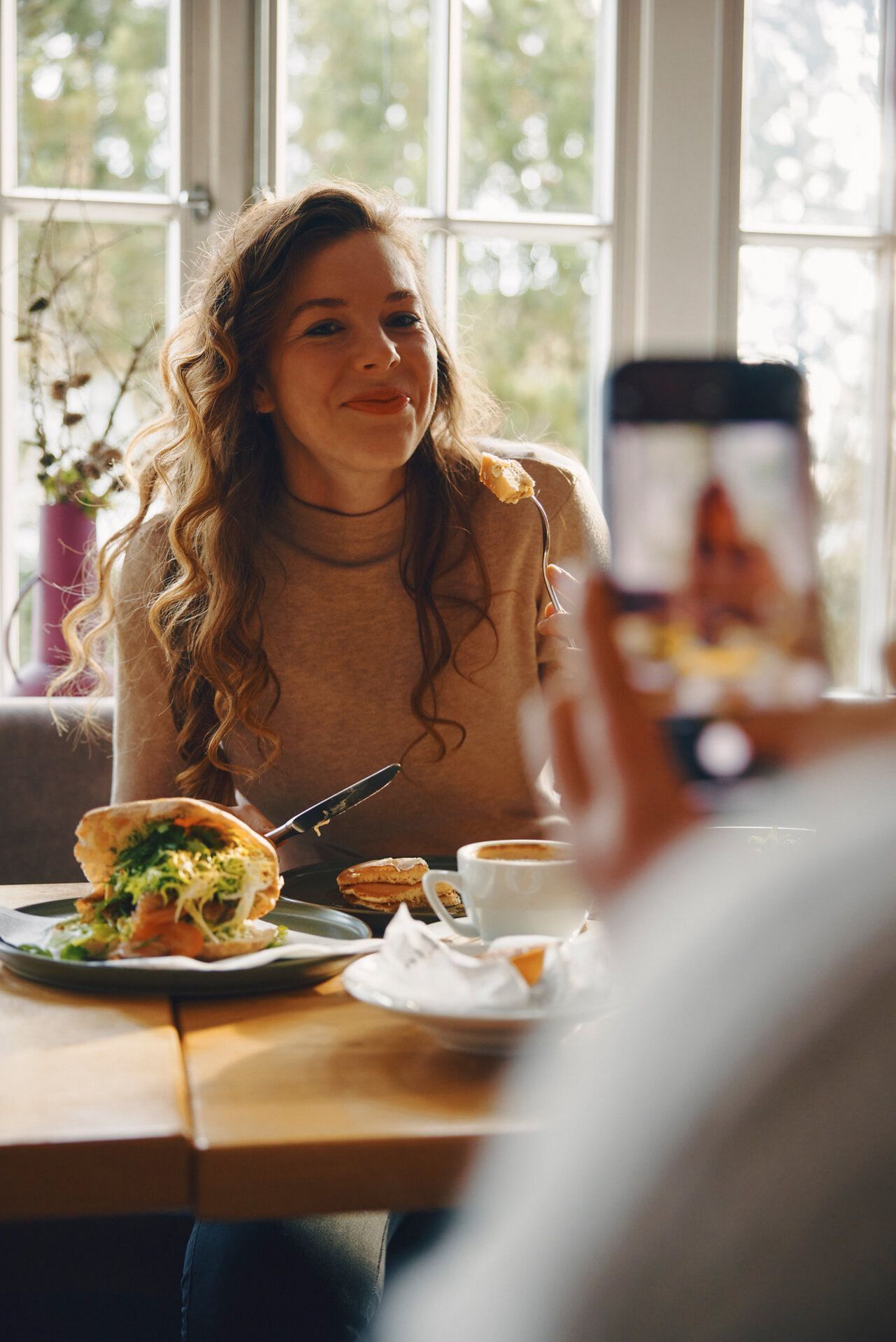 Frau lächelt beim Frühstück in einem Café, wird fotografiert