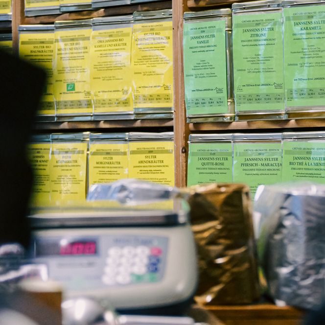 Grüne Teedosen mit Beschriftung dicht nebeneinander im Holzrega