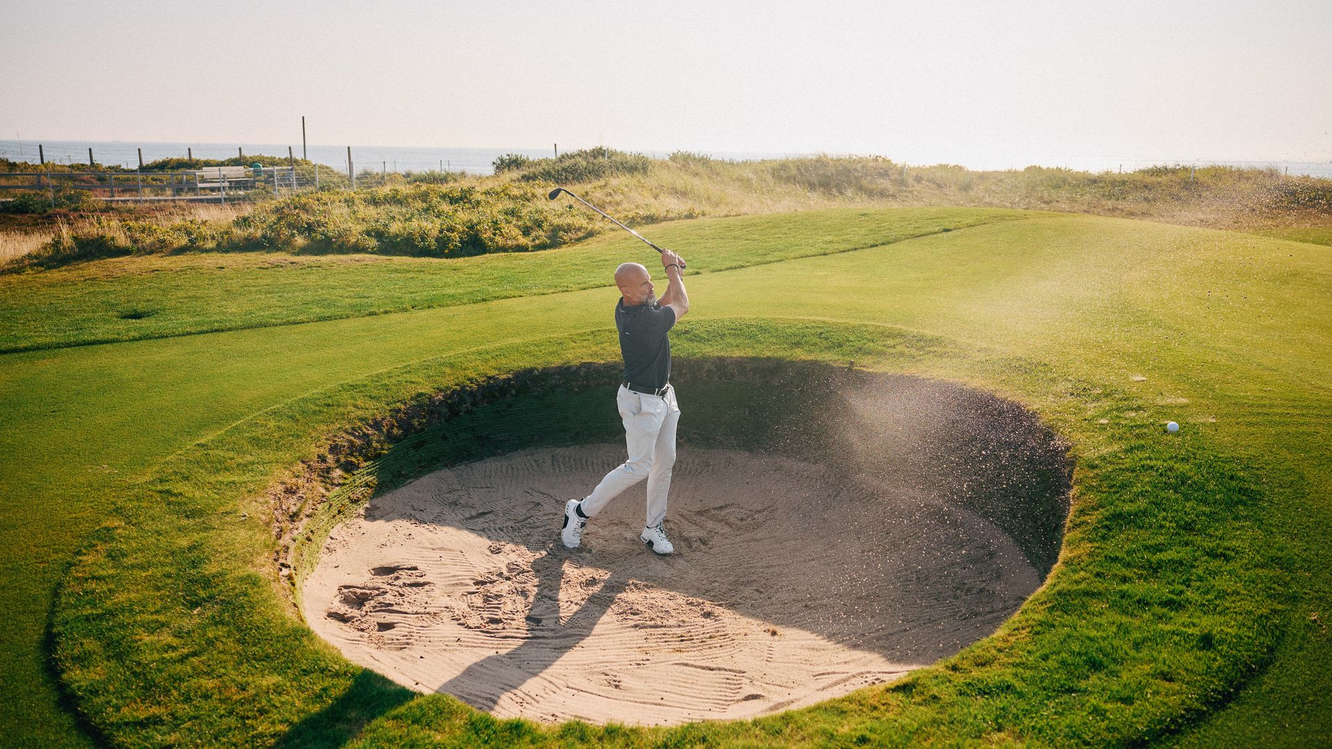 Golfer spielt aus einem Sandbunker auf einem sonnigen Golfplatz