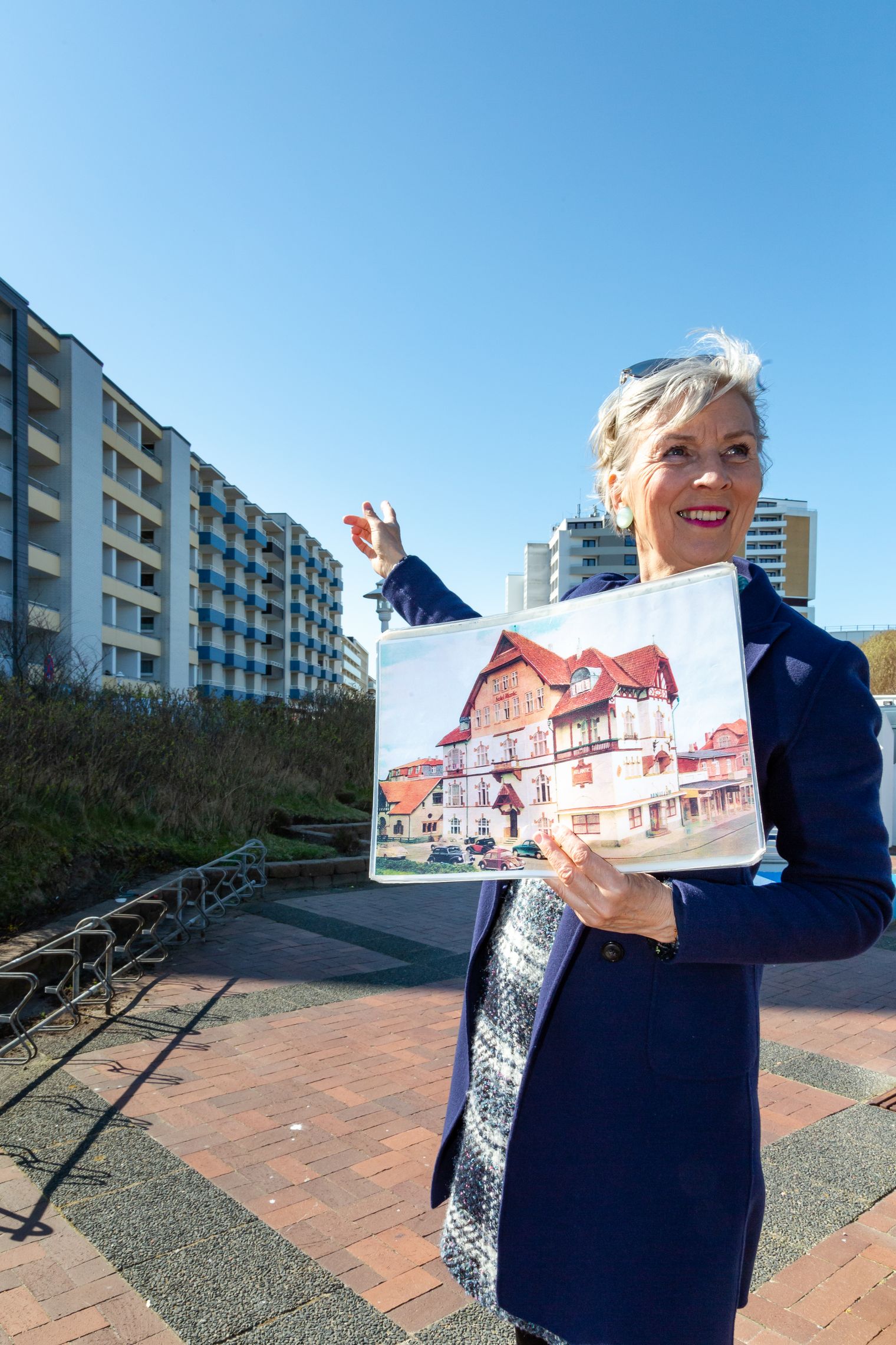 Frau hält ein historisches Foto und zeigt auf Gebäude in Westerland.