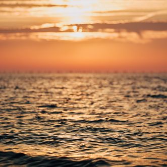 Ein Sonnenuntergang über der Nordsee, die goldenen Wellen reflektieren das warme Licht der untergehenden Sonne, während der Himmel in Orange- und Gelbtönen leuchtet.
