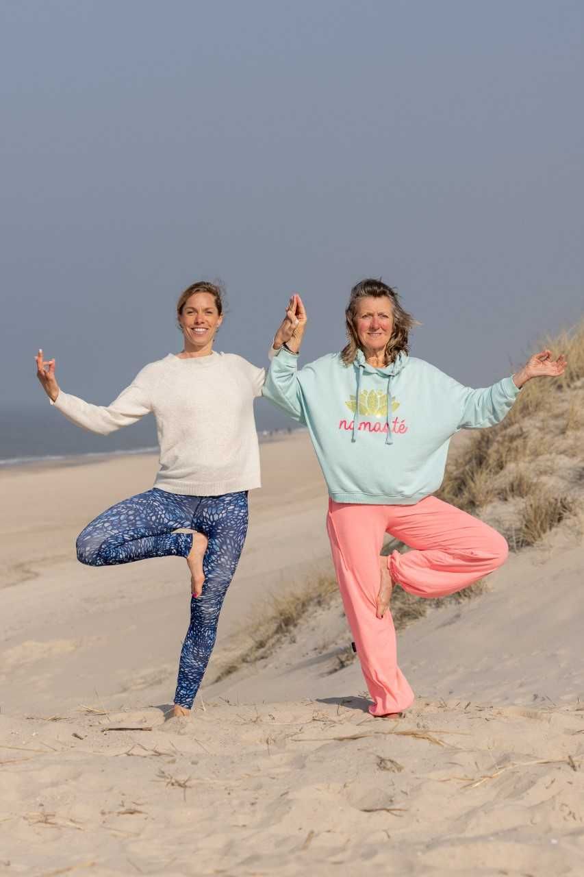 Zwei Yogalehrerinnen stehen im Asana Baum am Strand