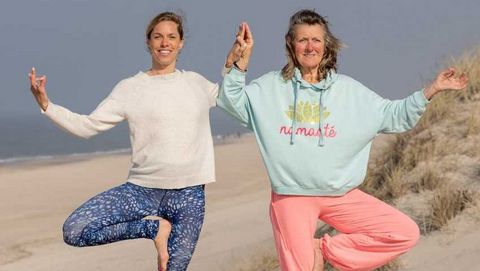 Zwei Yogalehrerinnen stehen im Asana Baum am Strand
