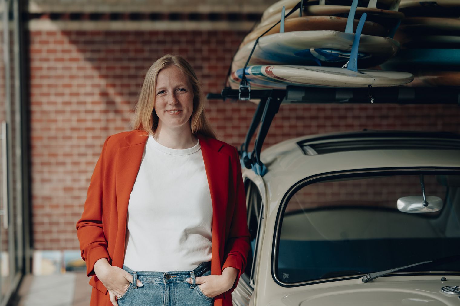 Kim Laura Horn von Sylt Marketing im roten Blazer vor einem Oldtimer mit Surfbrettern auf dem Dach.